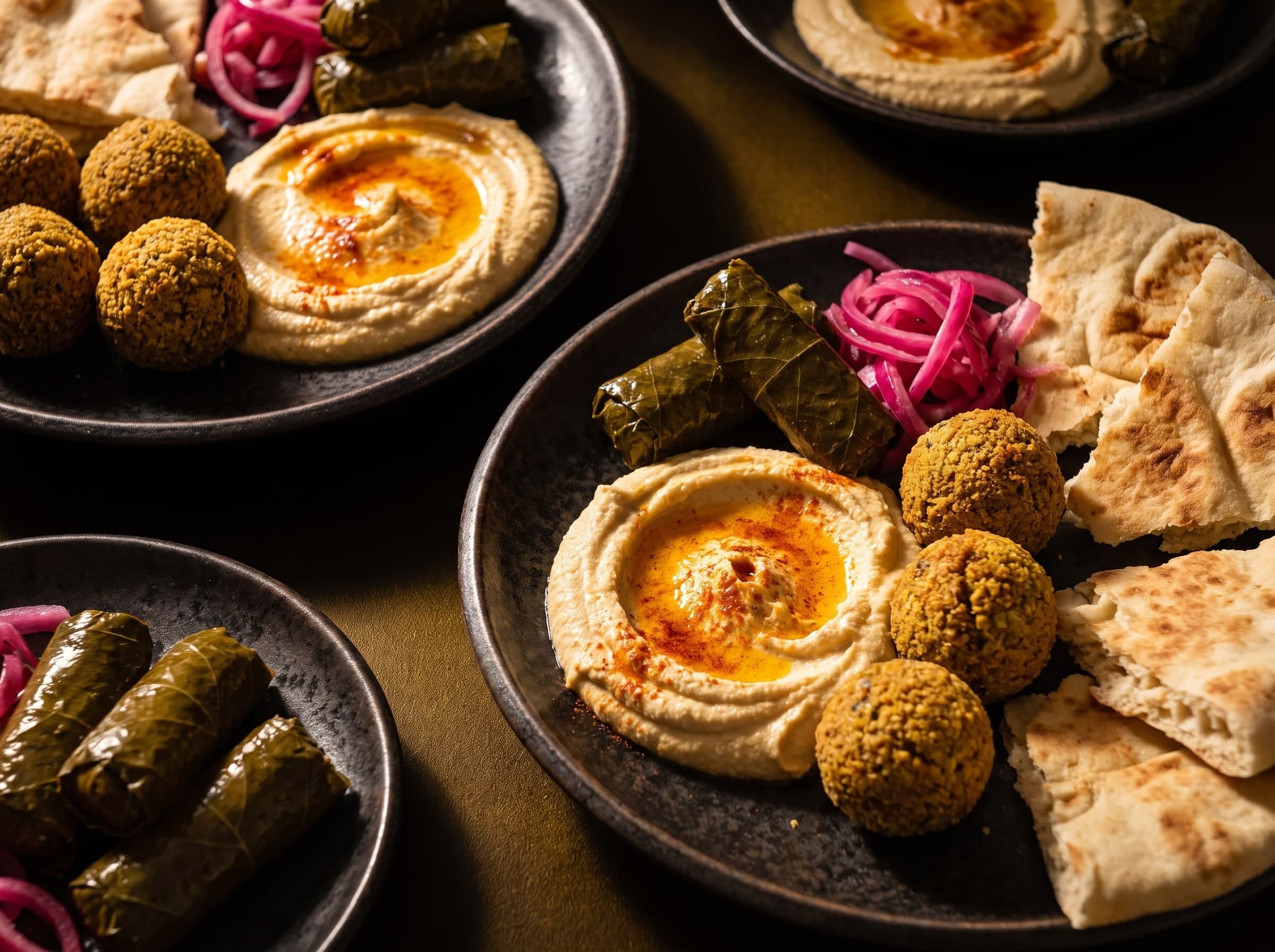 Houmous à l’huile de paprika, falafels, feuilles de vigne farcies, oignons marinés et pain pita sur des assiettes sombres